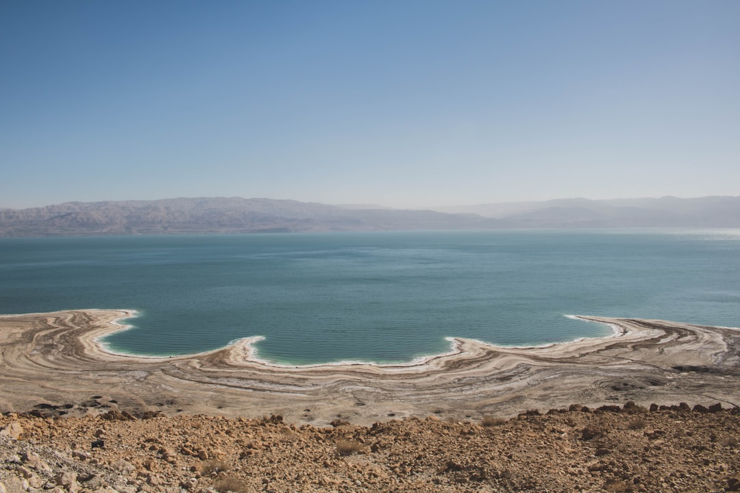 קבוצת מטיילים צועדת בשביל מדברי עם תצורות סלע ייחודיות, ובמרחק נראים אנשים נהנים מפעילות מים בים המלח.