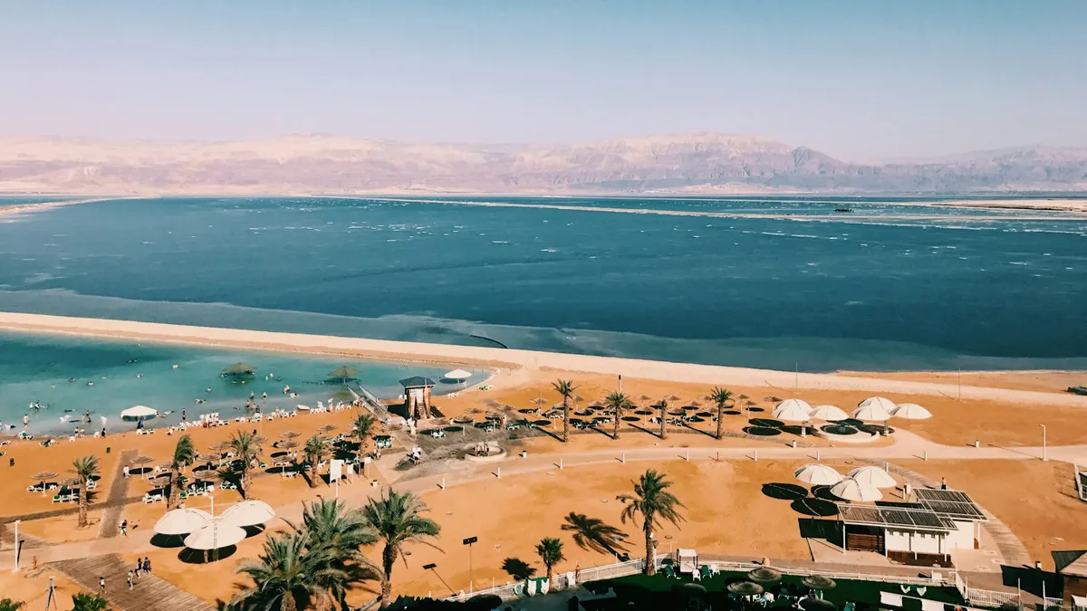 אוהל גלמפינג מפואר מואר בלילה במדבר, עם נוף לשמיים זרועי כוכבים ורמז לים המלח ברקע
