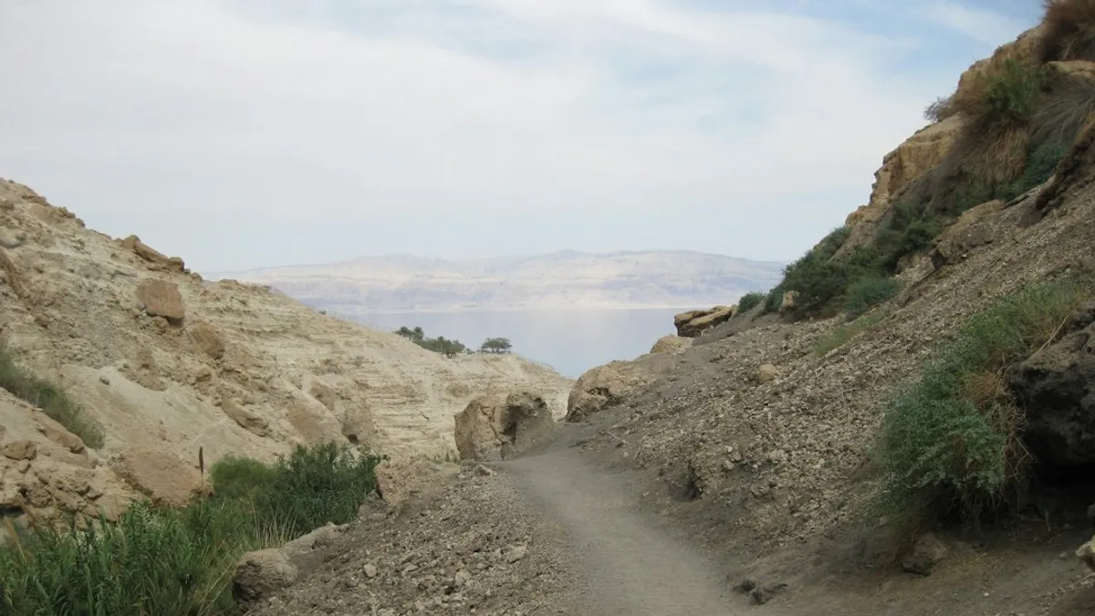 קבוצת מטיילים צועדת בשביל בשמורת טבע מדברית בים המלח, עם נוף עוצר נשימה ונווה מדבר רחוק.